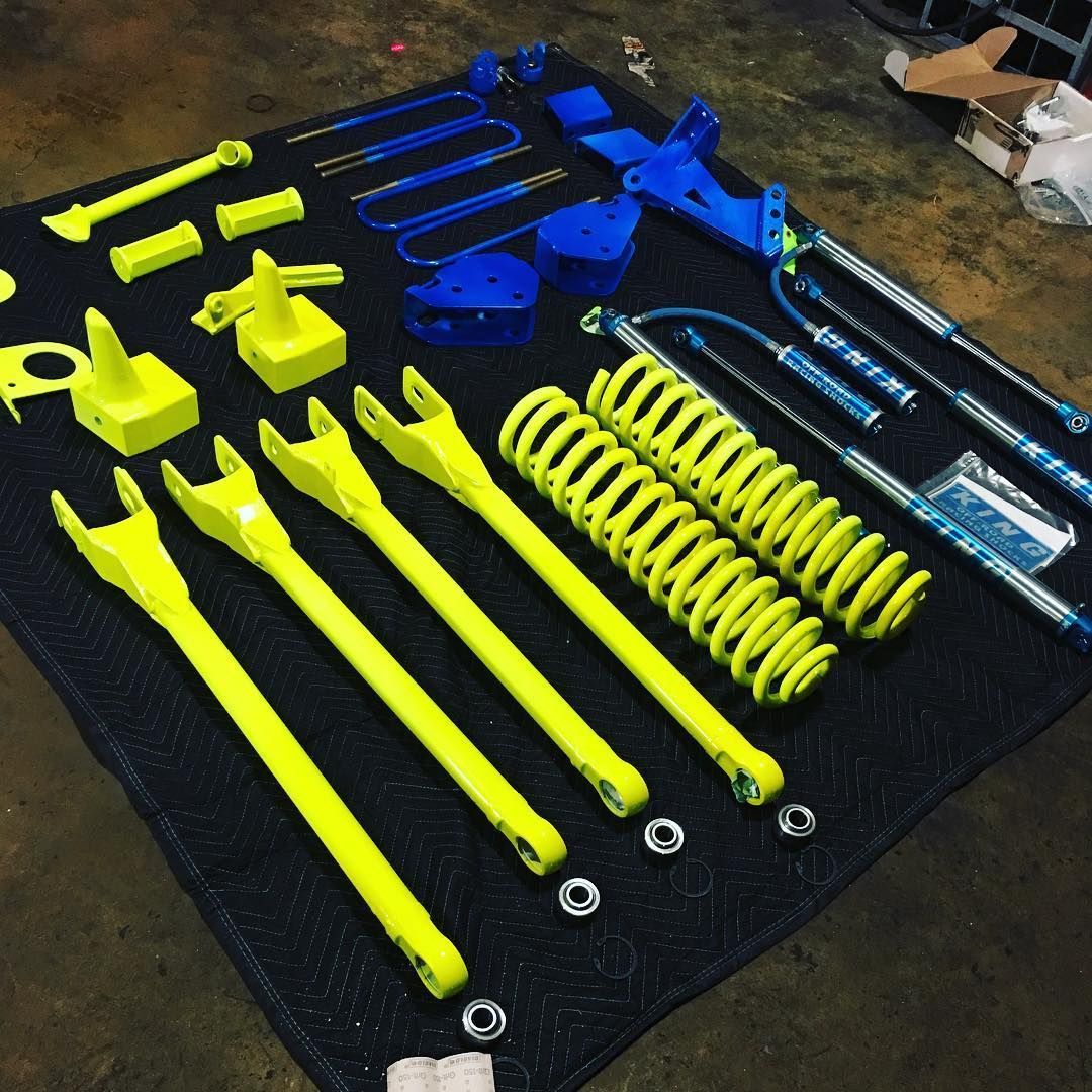 Assorted yellow, blue, and black vehicle suspension components laid out on a floor.
