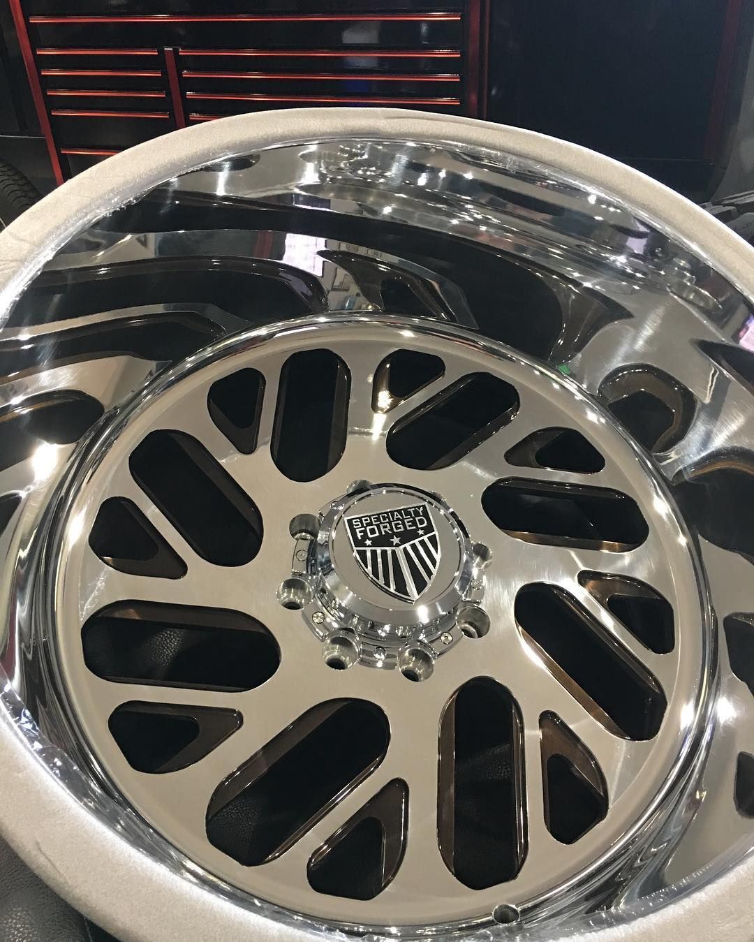 Chrome car wheel rim with black cutout spokes and a shield-shaped center cap on a dark background