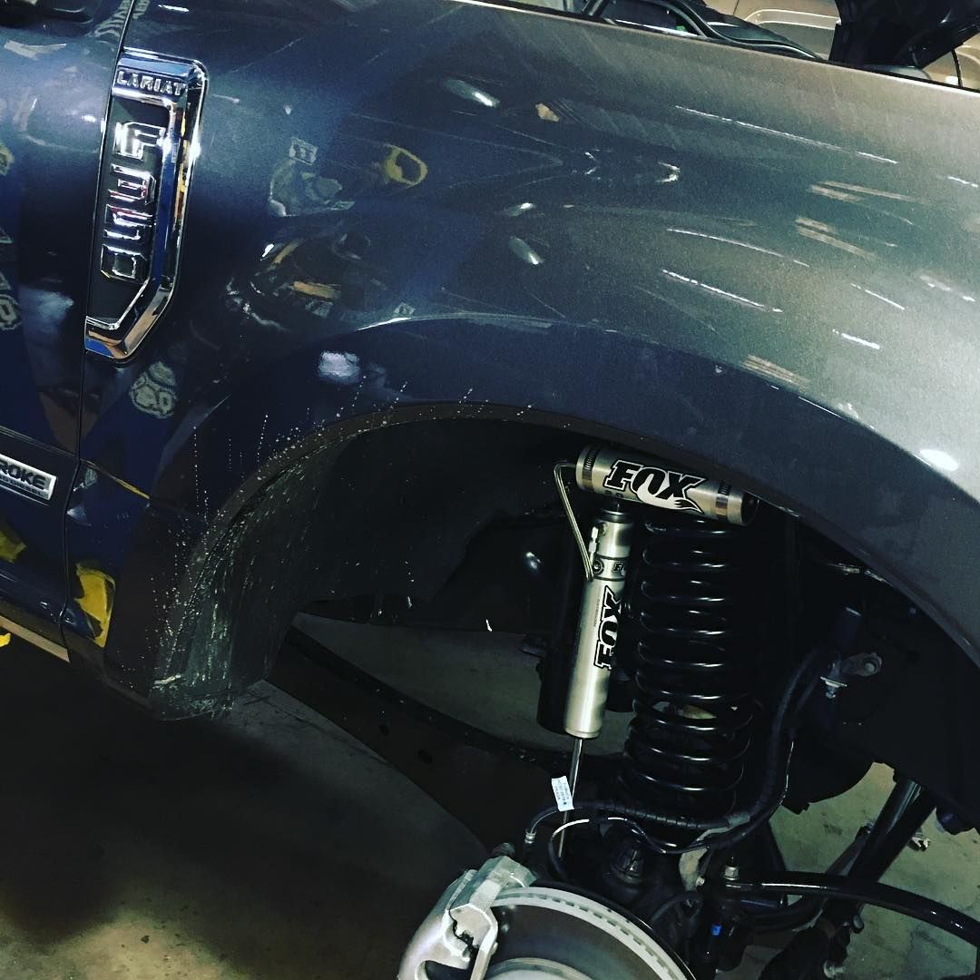 Close-up of a dark blue truck’s front wheel well, showing a black coilover suspension and chrome trim