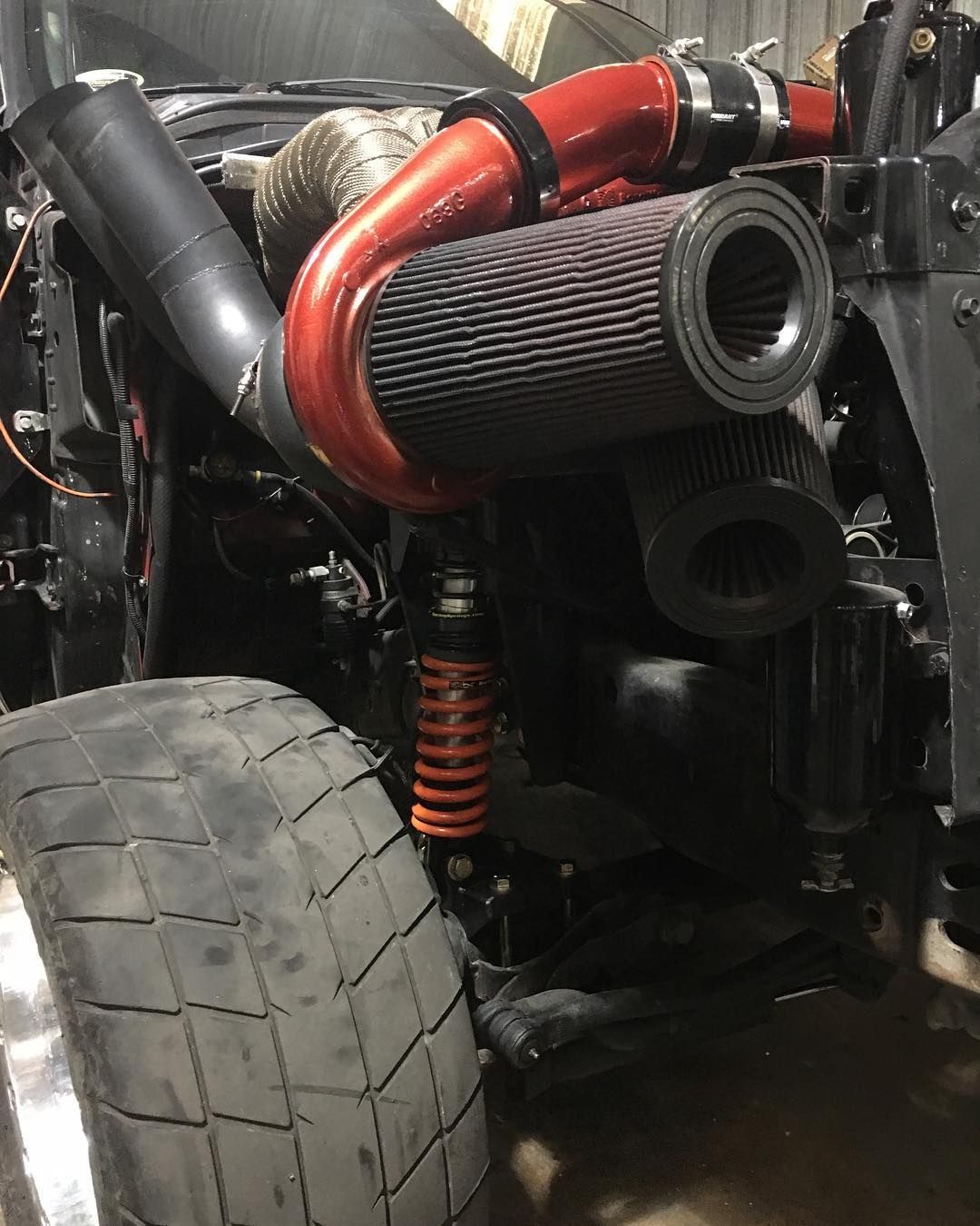 Close-up of a racing car’s rear suspension, tire, and red intake piping in a workshop.