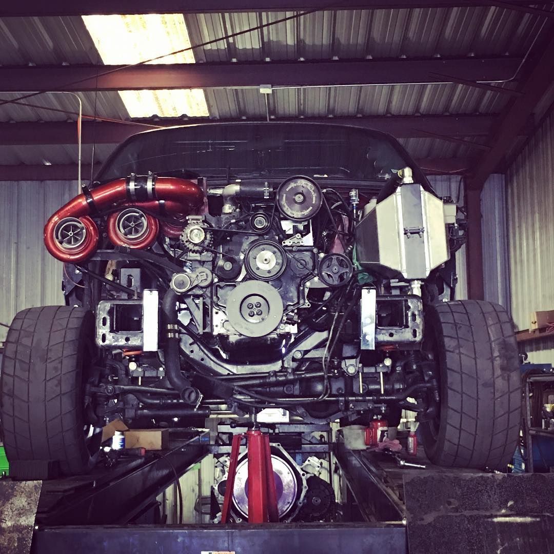 Rear view of a race car chassis with exposed engine and wide tires inside a garage.
