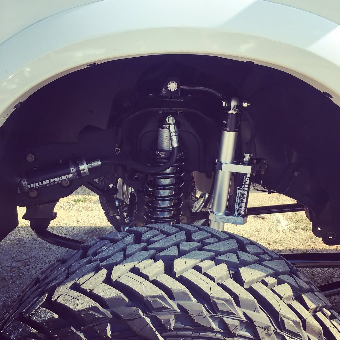 Truck suspension and large off-road tire under a white fender, viewed from below