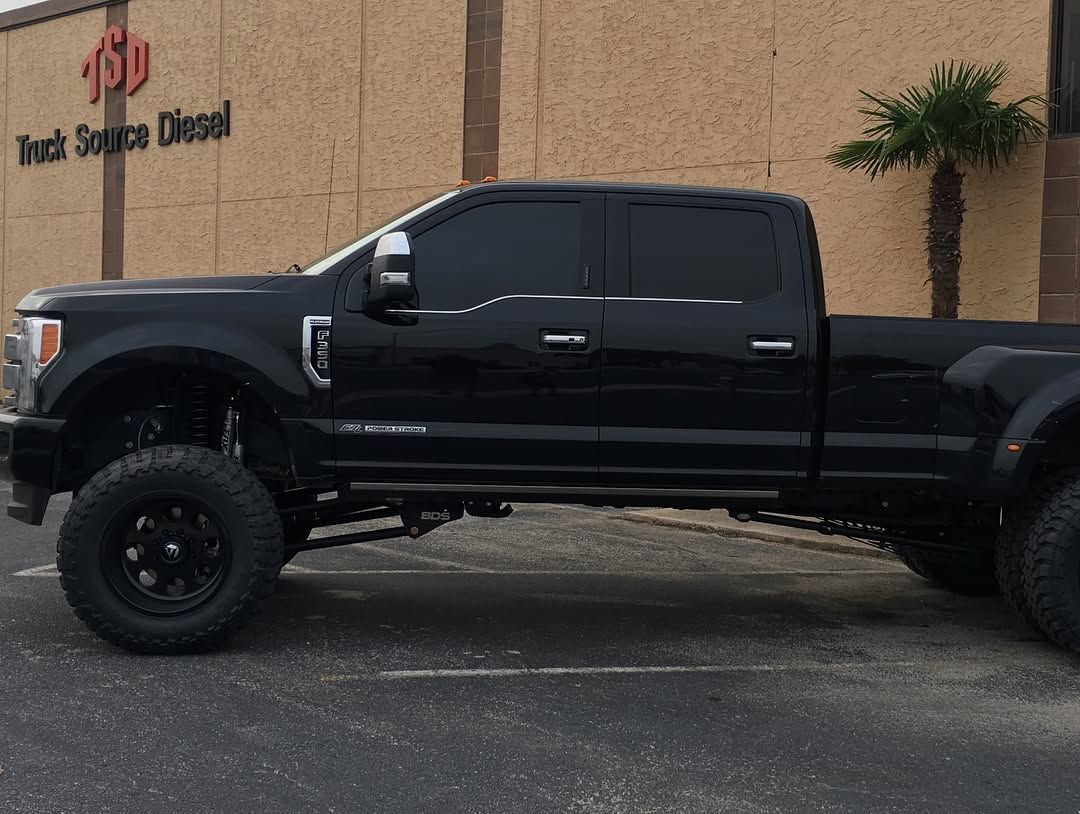 Black lifted pickup truck parked outside a beige building with palm trees