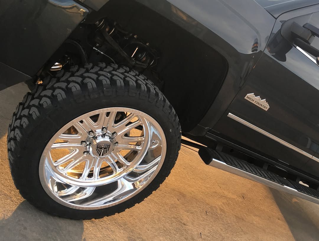Close-up of a black truck’s chrome wheel and tire on a showroom floor.