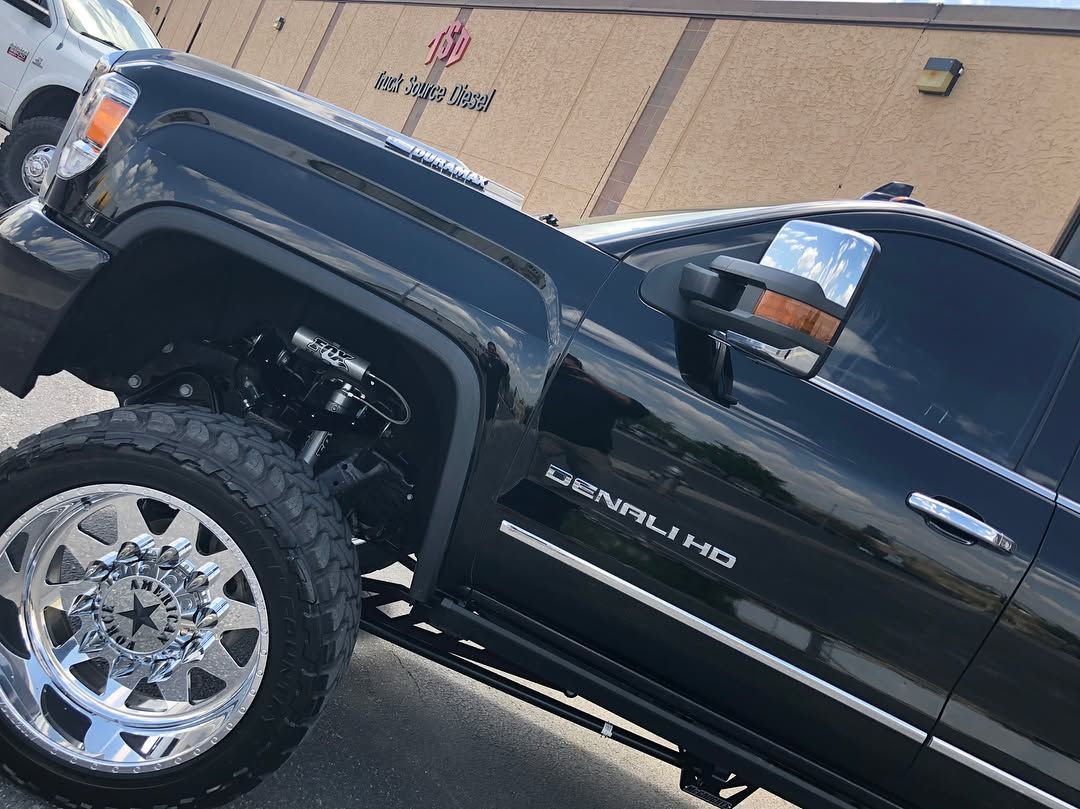 Lifted black GMC truck with chrome wheels parked in front of a building.