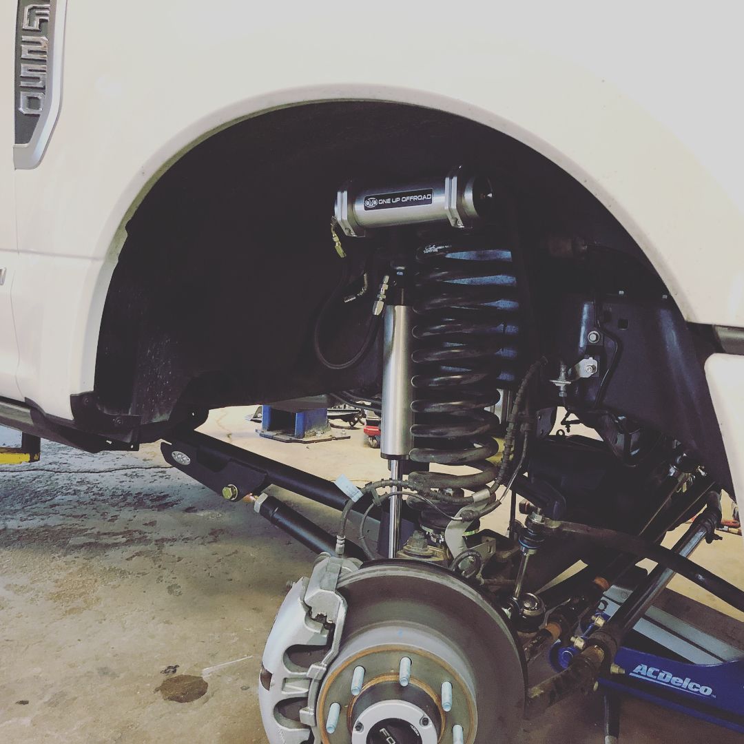 White off-road truck wheel well with exposed suspension and brake assembly, showing lifted front axle.