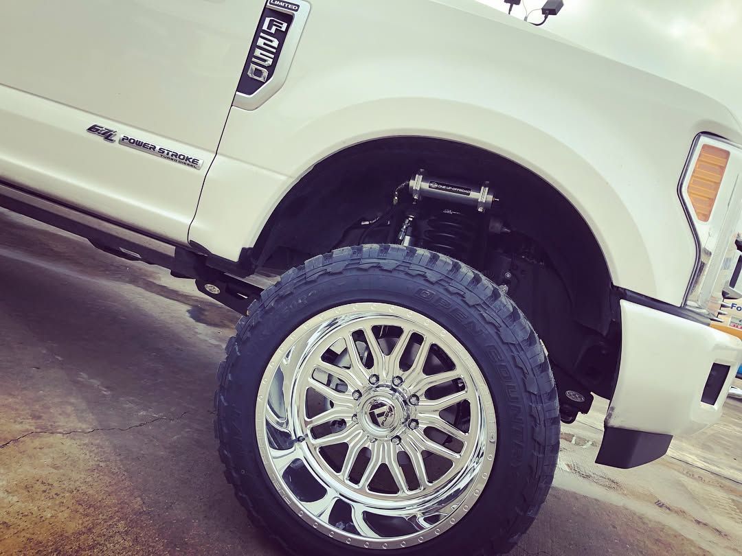 White lifted truck with chrome wheel and large off-road tire shown in close-up.