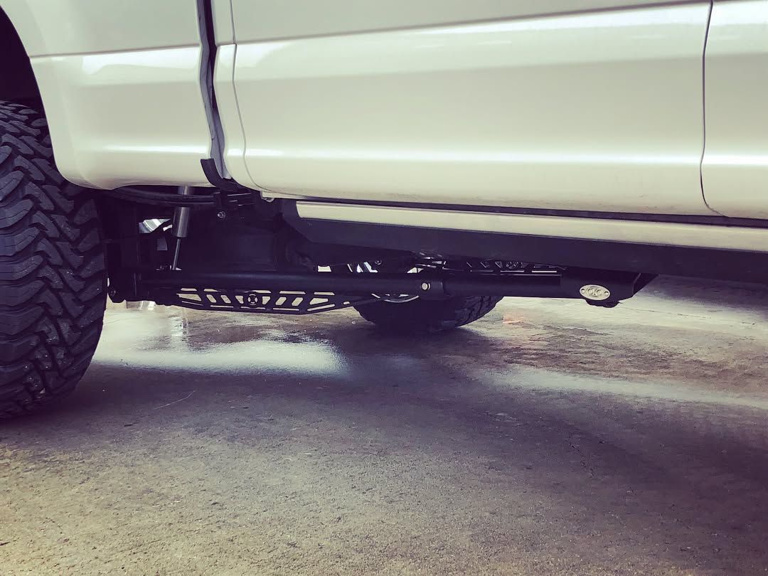 White truck side panel with a dangling purple strap, showing the undercarriage and large rear tire on pavement