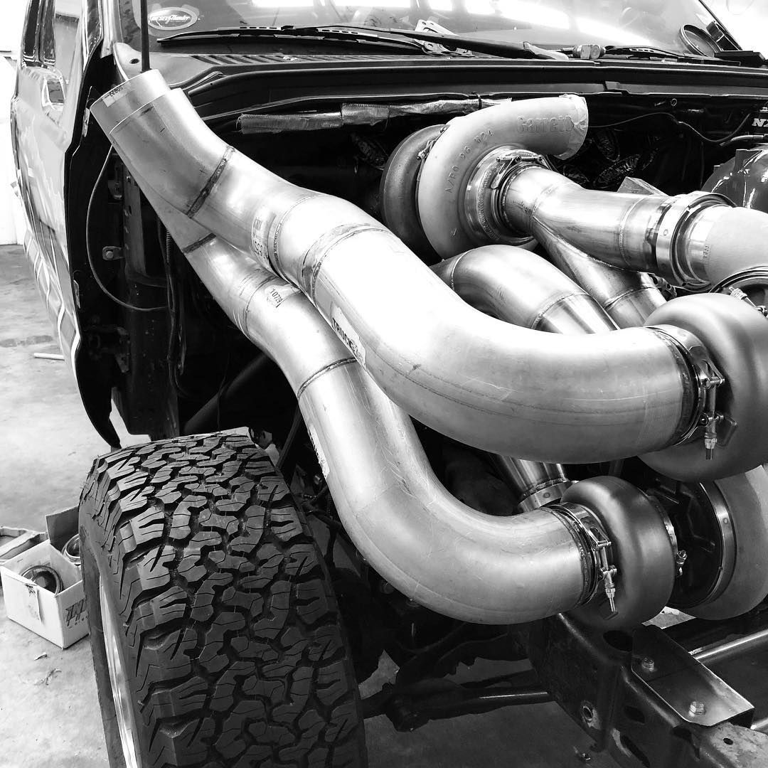 Shiny exhaust pipes and a large off-road tire on a vehicle in a garage