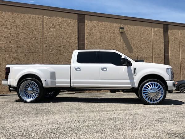 White pickup truck with oversized chrome rims parked beside a tan building.