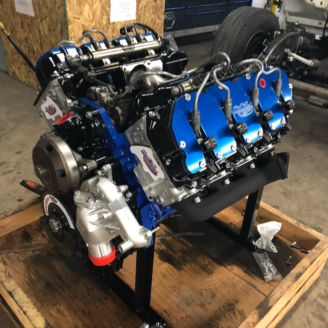 Blue-and-black V8 engine on a wooden pallet in a workshop setting