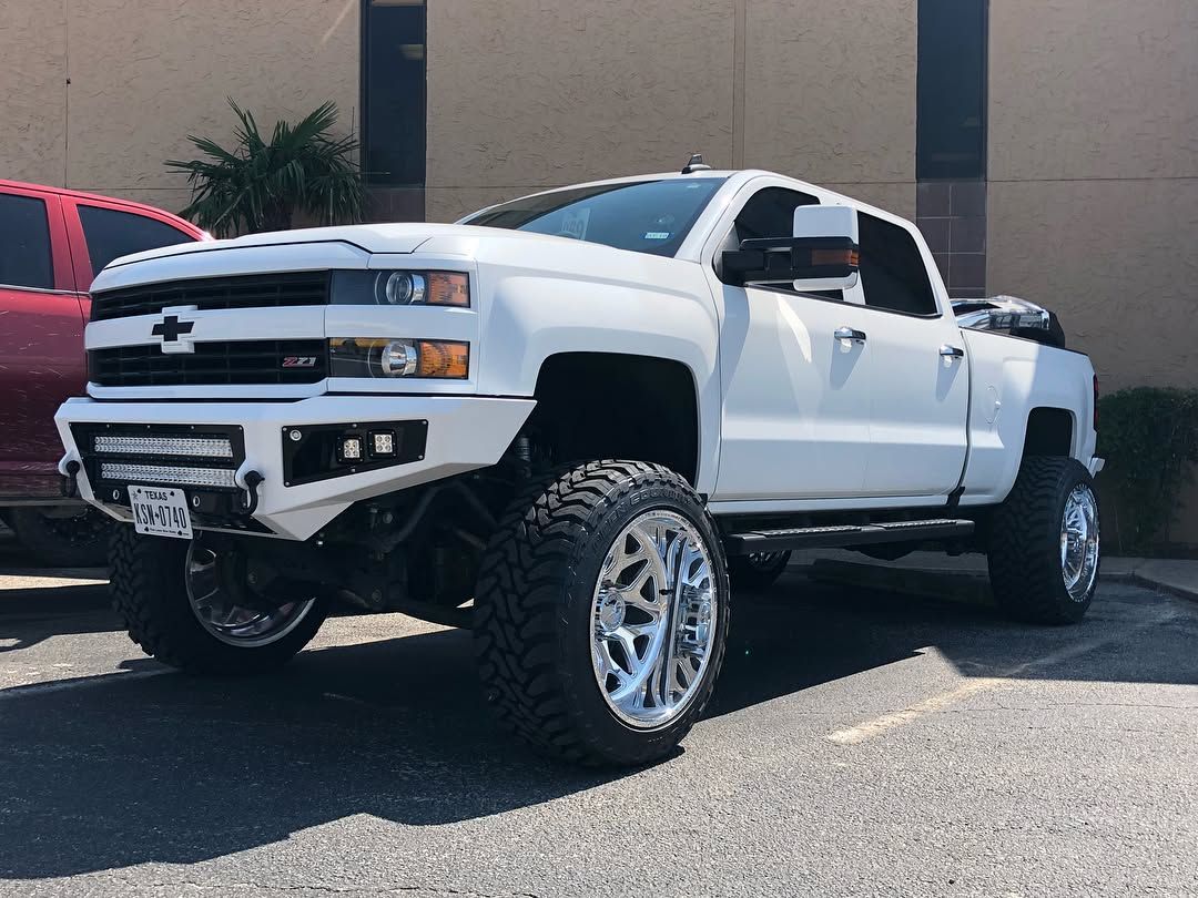 White lifted Chevrolet pickup truck parked outdoors beside a red vehicle.