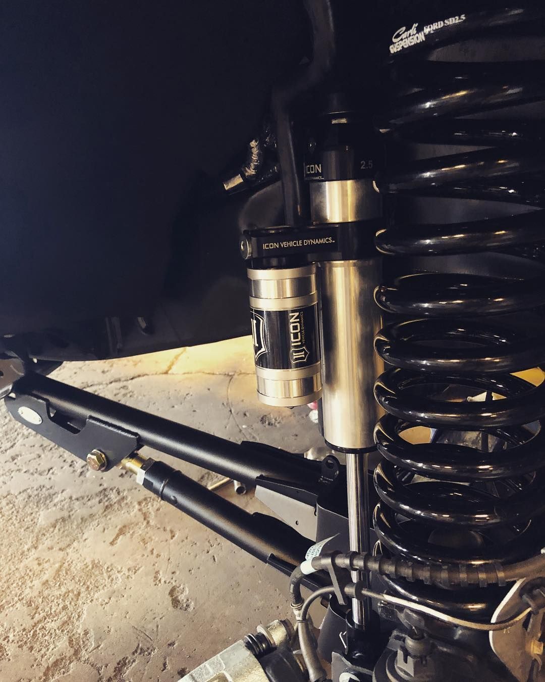 Close-up of a black and silver motorcycle rear suspension with spring and shock absorber on a sandy surface
