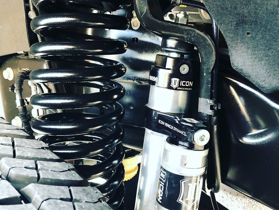 Close-up of a black coil spring and silver shock absorber on an off-road vehicle suspension.