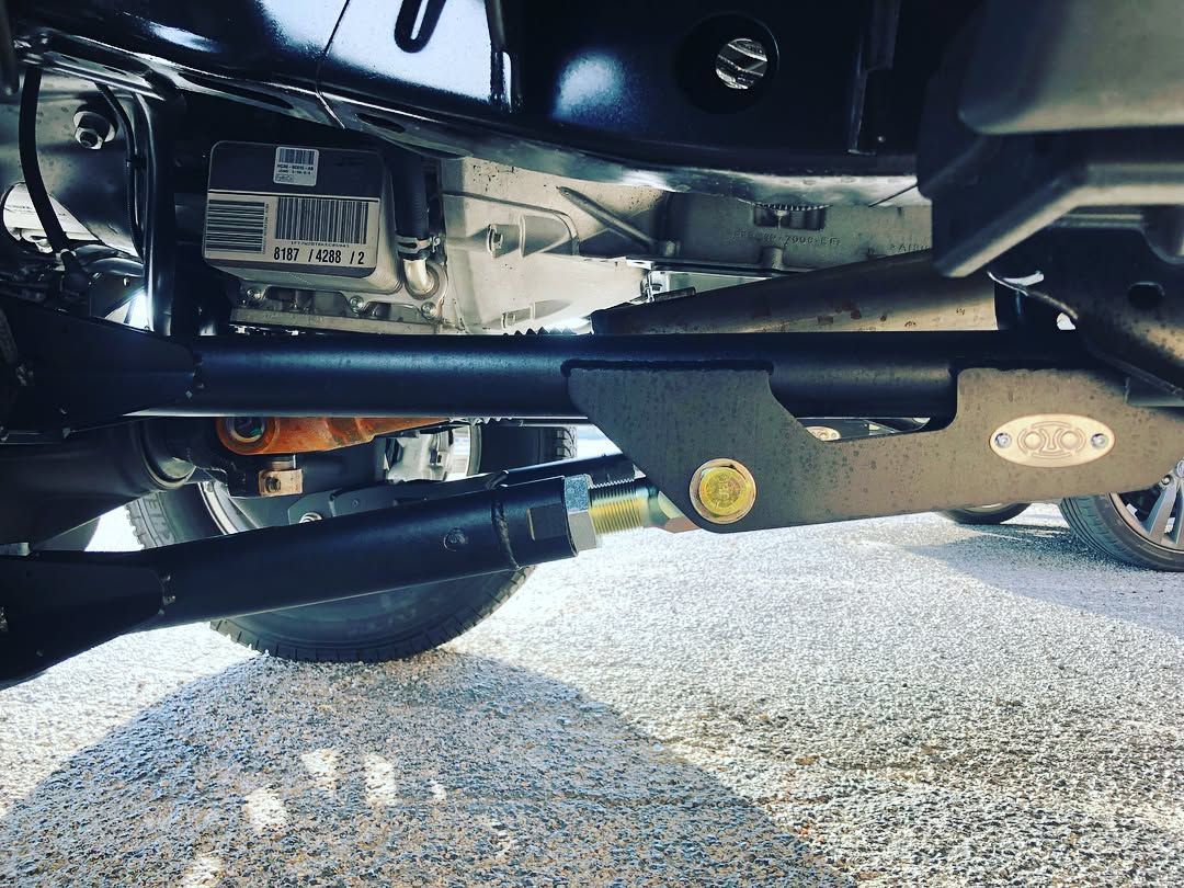 Undercarriage of a vehicle showing suspension, axle, and exhaust components over gravel.