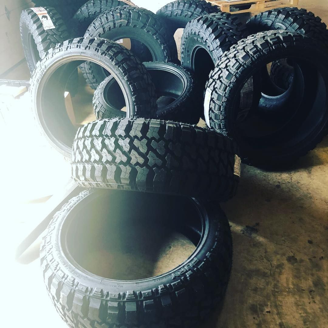 Several black off-road tires stacked and scattered on a concrete floor.