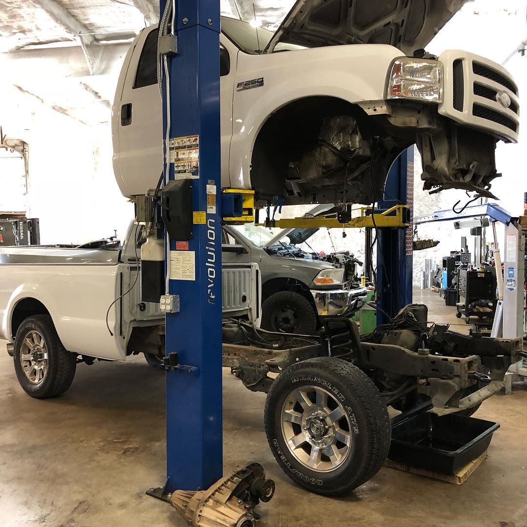 White pickup truck in an auto shop on a lift, with its front end removed during repair.