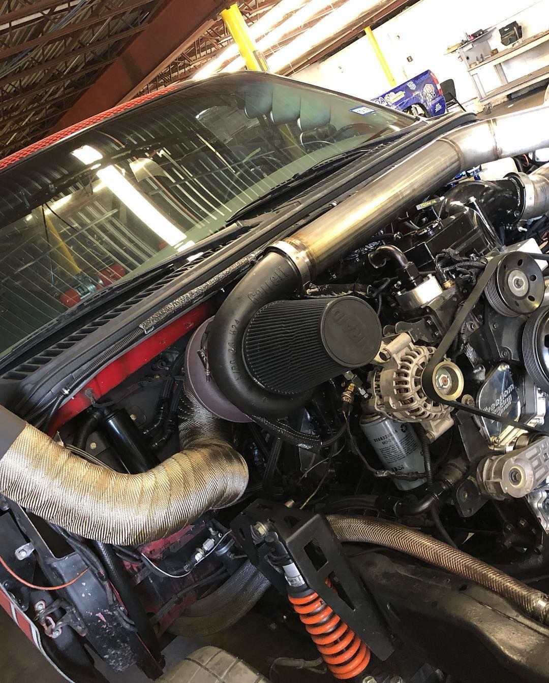 Close-up of a modified car engine bay with exposed hoses, belts, and a black air intake.