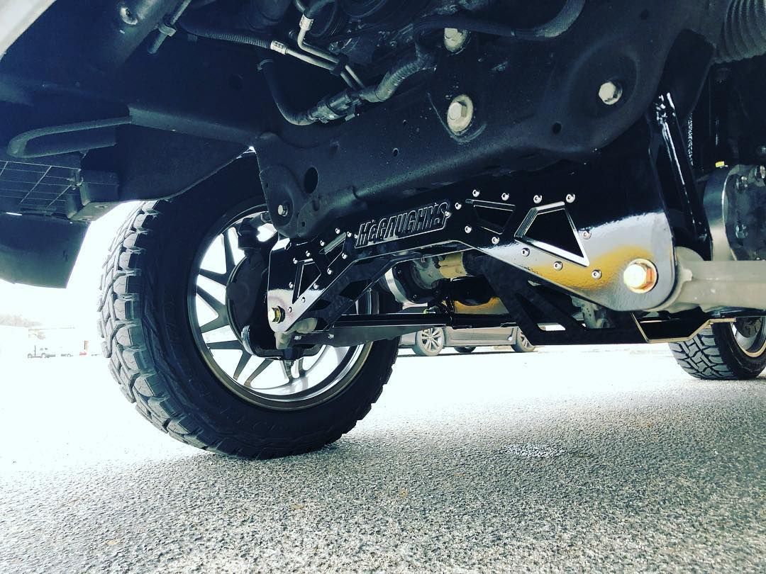 Undercarriage view of a black vehicle with a rear wheel and suspension on a gravel surface
