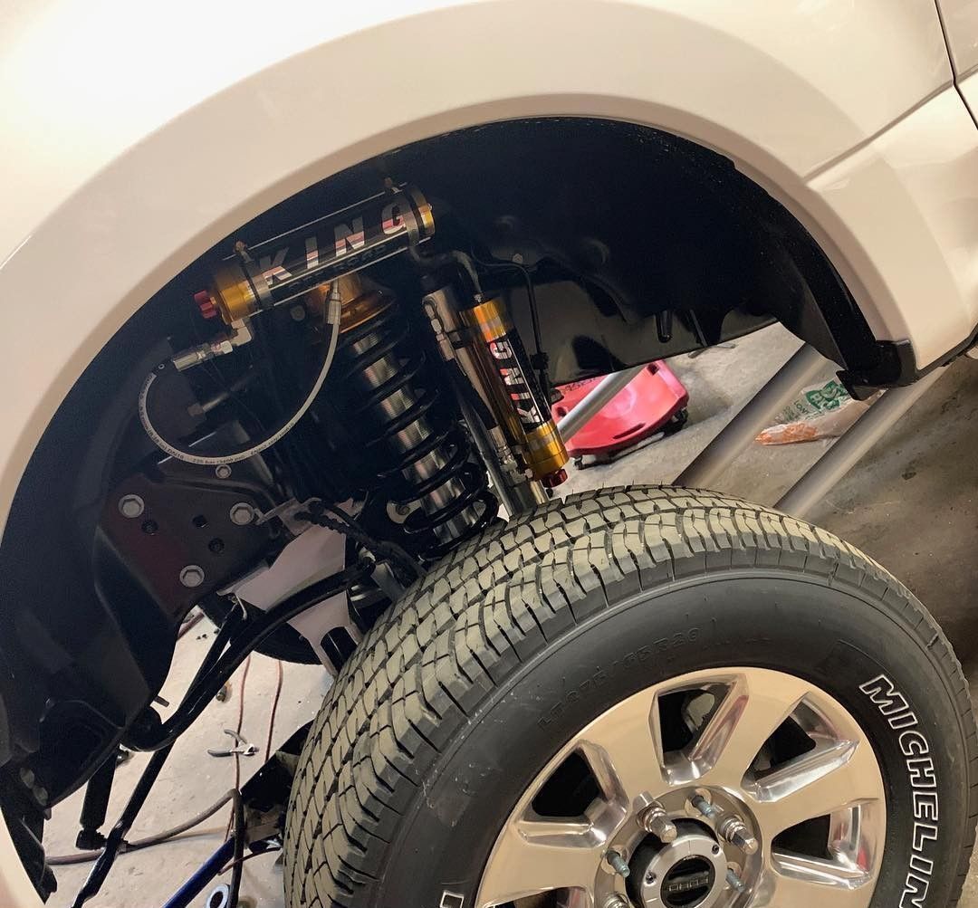 Truck wheel well showing suspension components and tire, with a beige body and chrome rim.