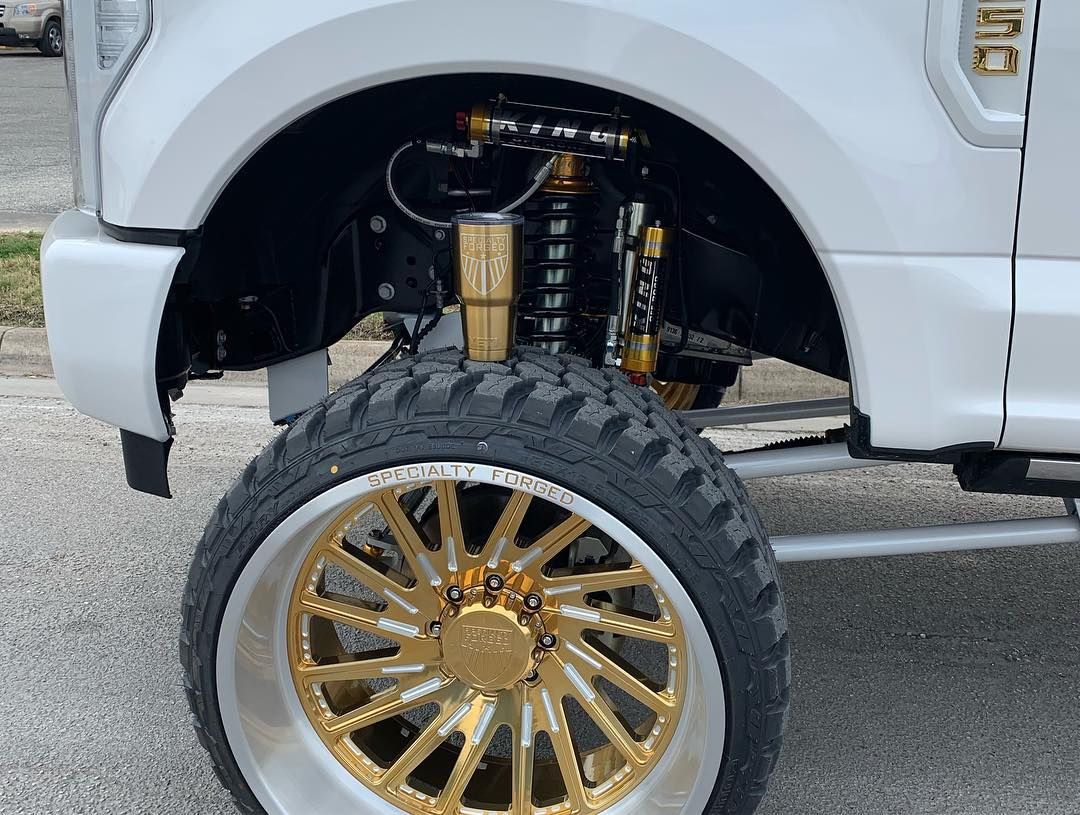White truck with gold rims and lifted suspension, close-up of front wheel and fender