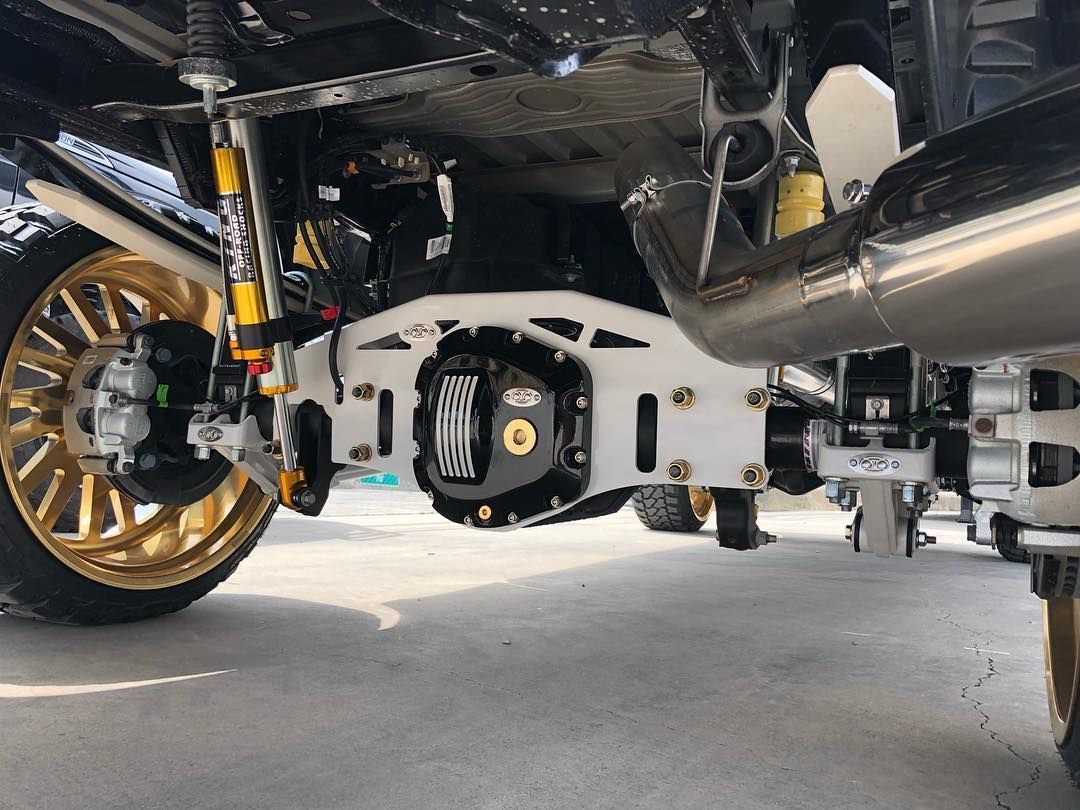 Undercarriage of a car showing suspension, exhaust, and gold alloy wheels in a workshop.