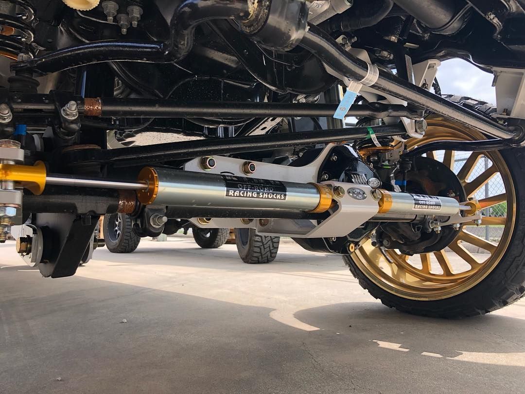 Low-angle view of a car’s undercarriage with chrome exhaust and gold wheels on pavement