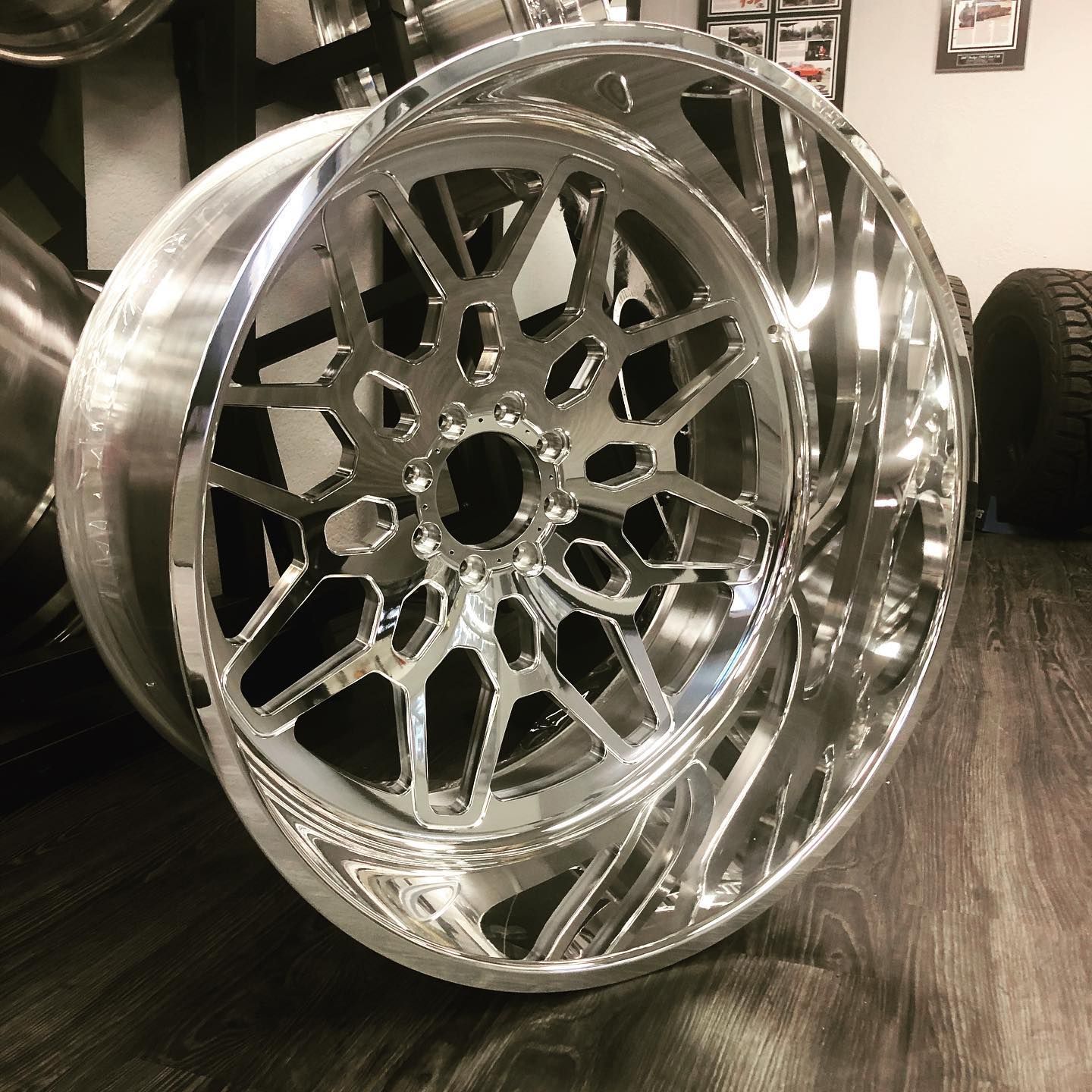 Shiny chrome alloy wheel rim with intricate spoke design, leaning upright in a garage.