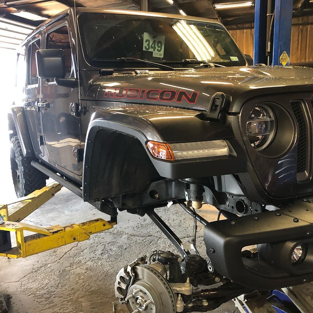 Gray Jeep Rubicon lifted on a shop jack with front suspension exposed in an auto repair garage