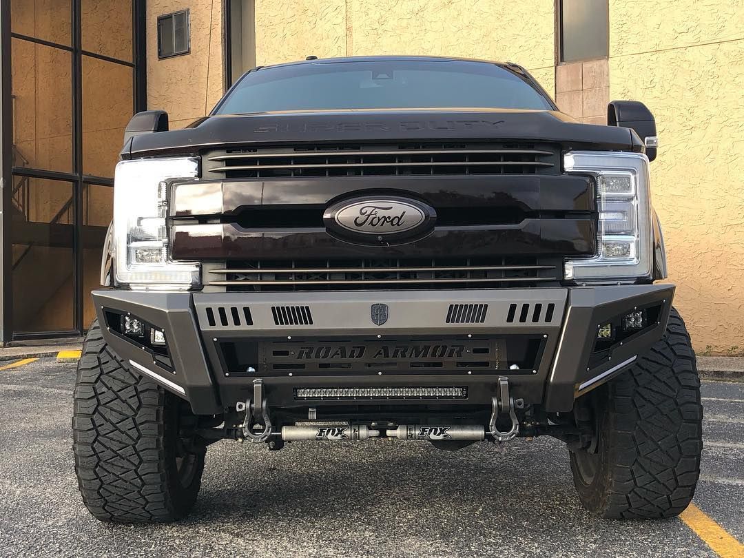 Front view of a lifted black Ford truck with off-road bumper parked on gravel near a building