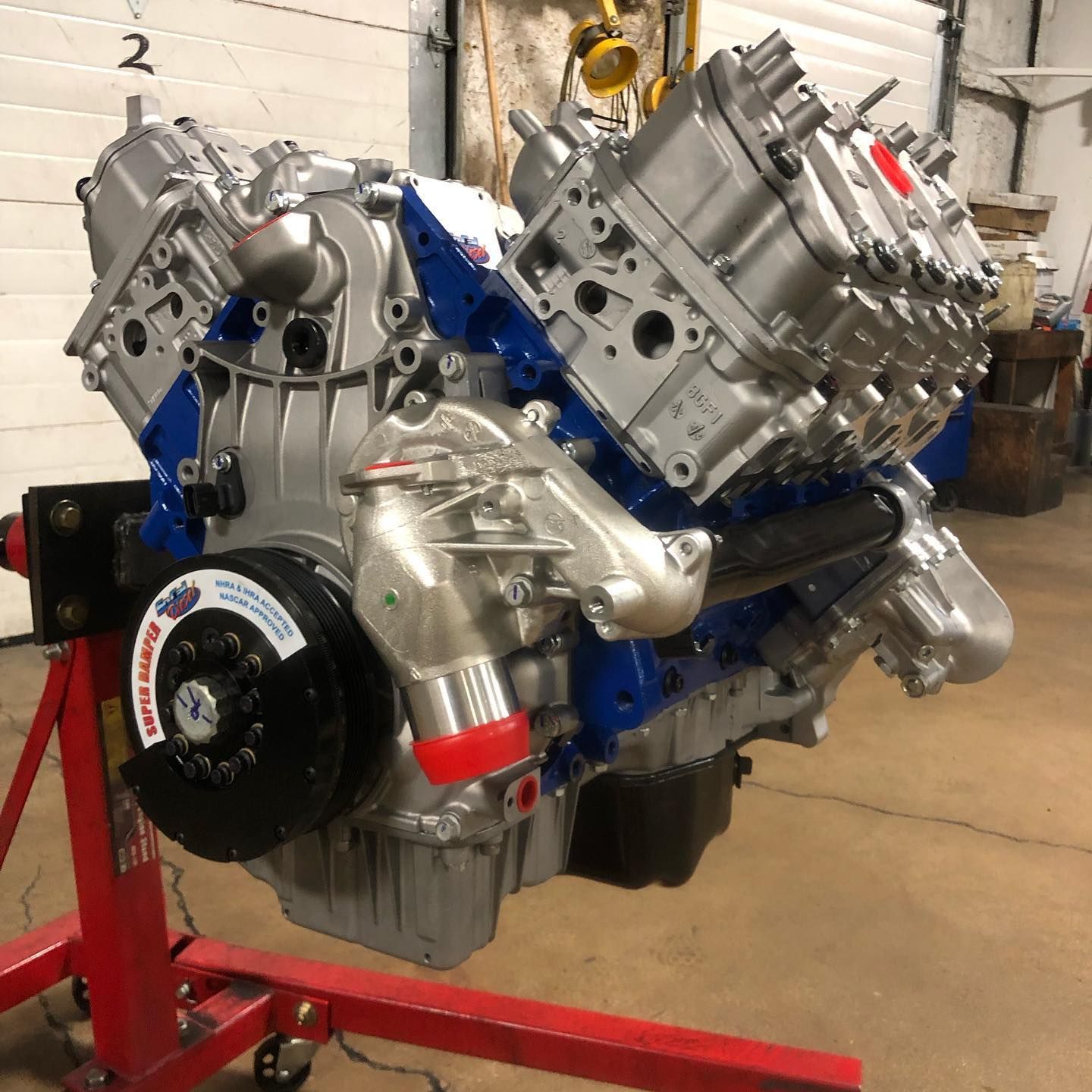 Shiny V8 engine on a red stand in a workshop, with silver and blue components exposed.