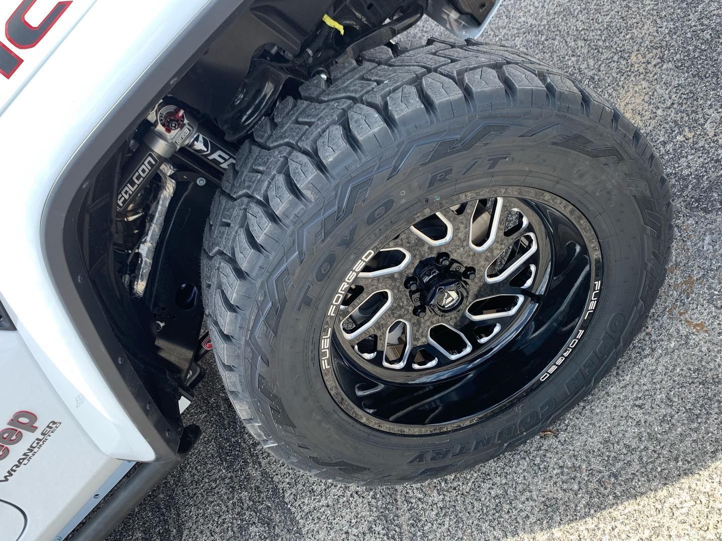 Close-up of a silver off-road truck’s front wheel with a rugged tire on pavement.