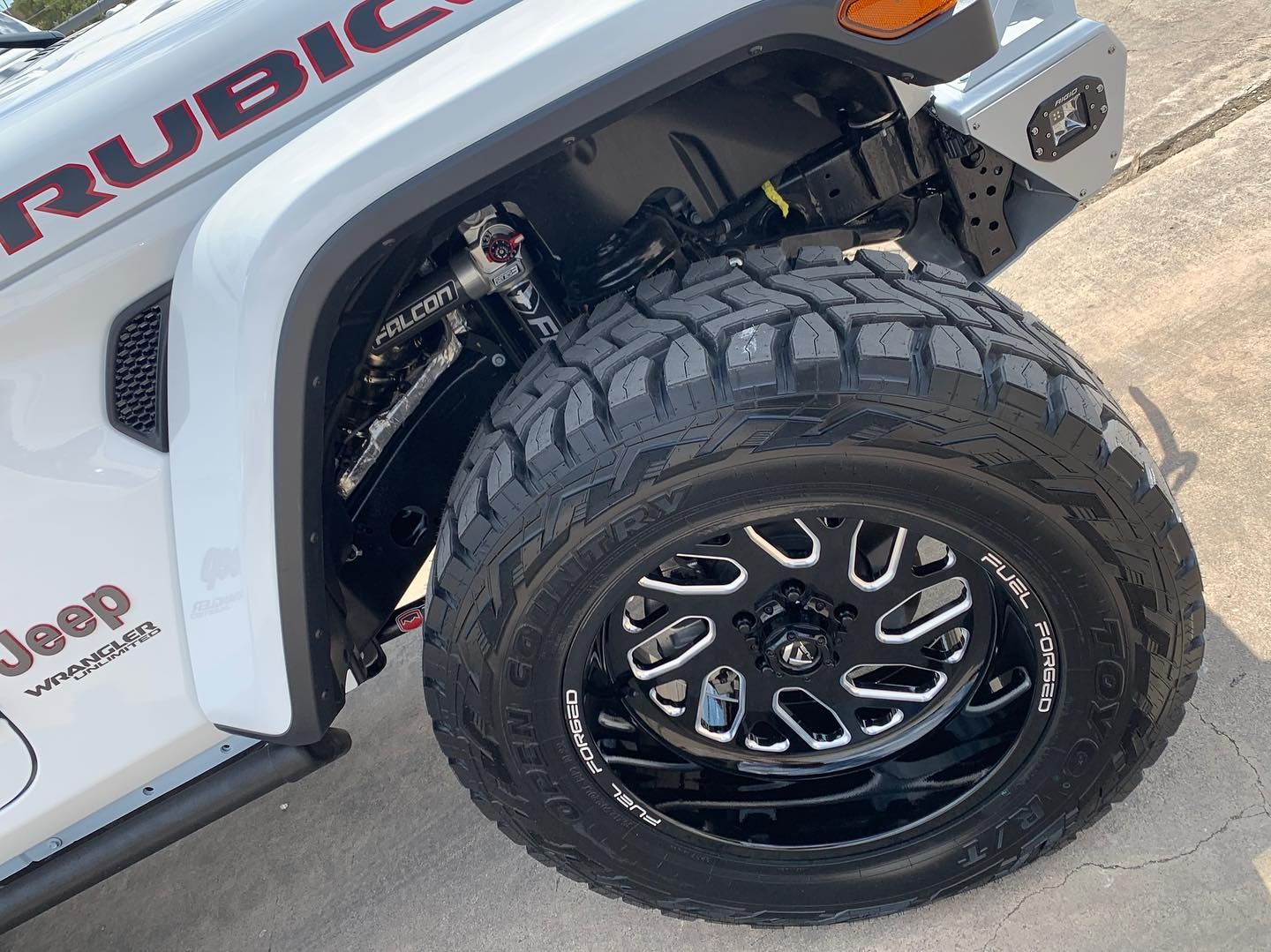 Close-up of a white Jeep Rubicon with a large off-road tire and black rim on a paved road.