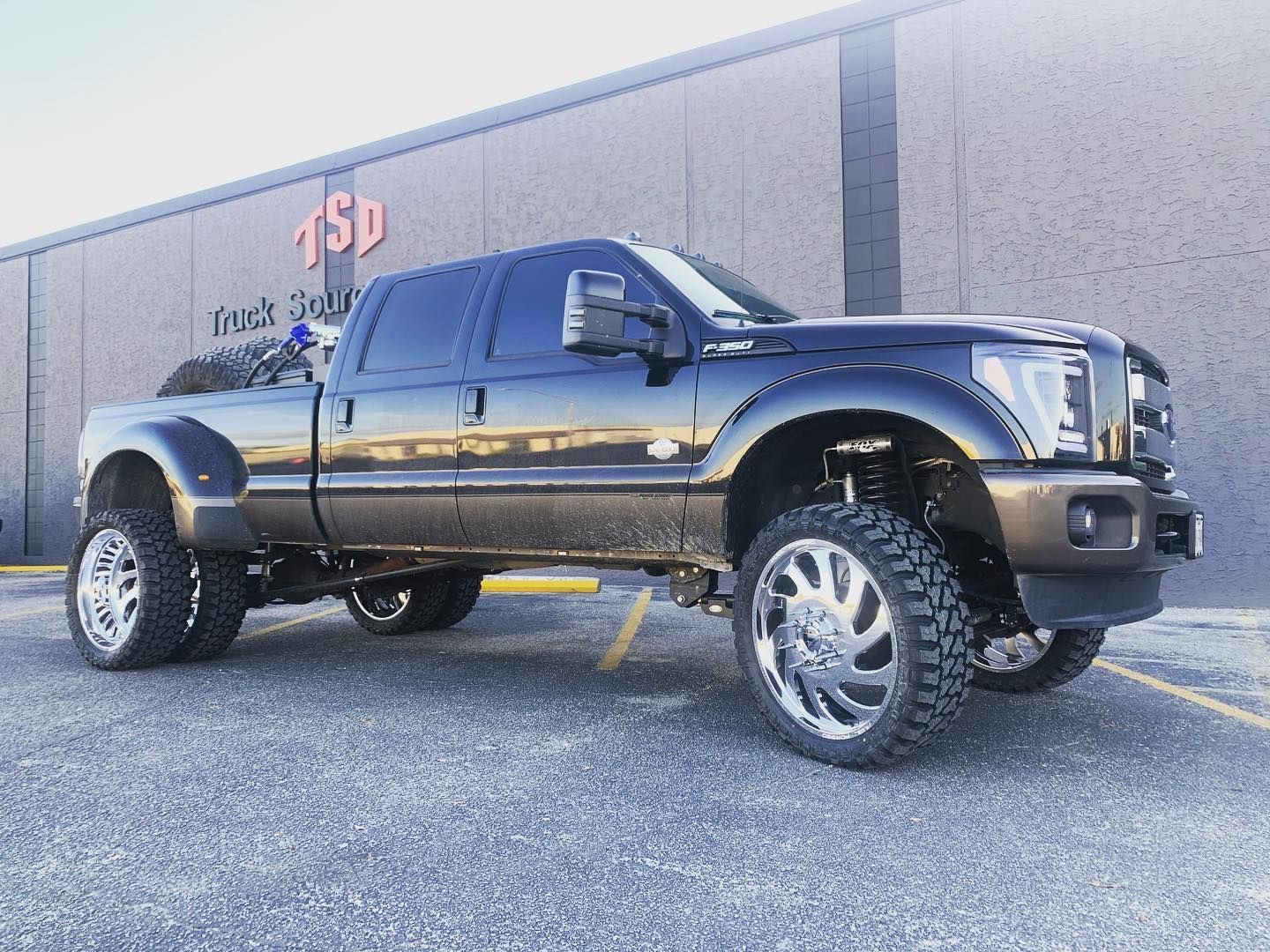 Lifted black pickup truck parked outside a building with a red sign