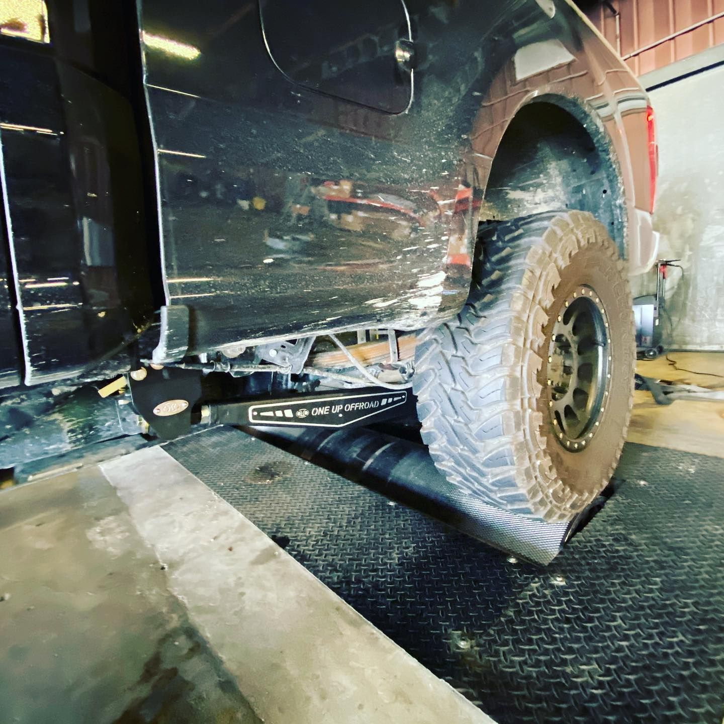 Mud-splattered off-road SUV on a lift in a workshop, with a large rear tire visible