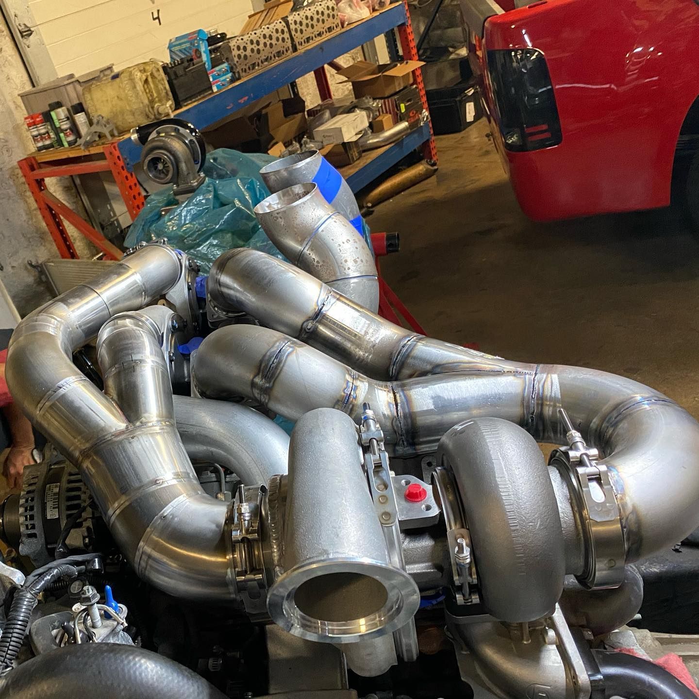 Silver turbo piping in a garage beside a red vehicle and shop equipment