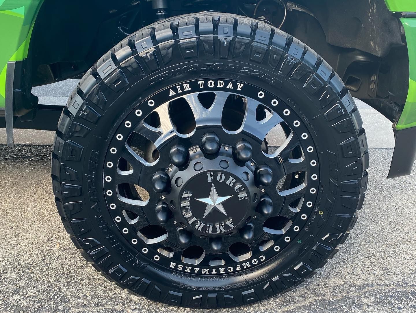 Close-up of a black off-road truck tire and rim with star hubcap on gravel