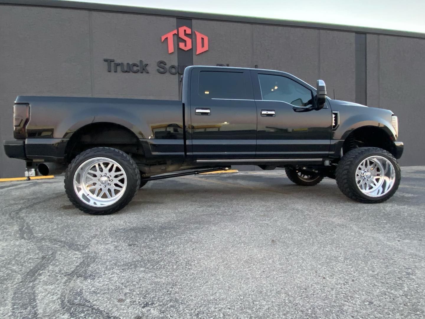 Black lifted pickup truck parked in front of a truck service building