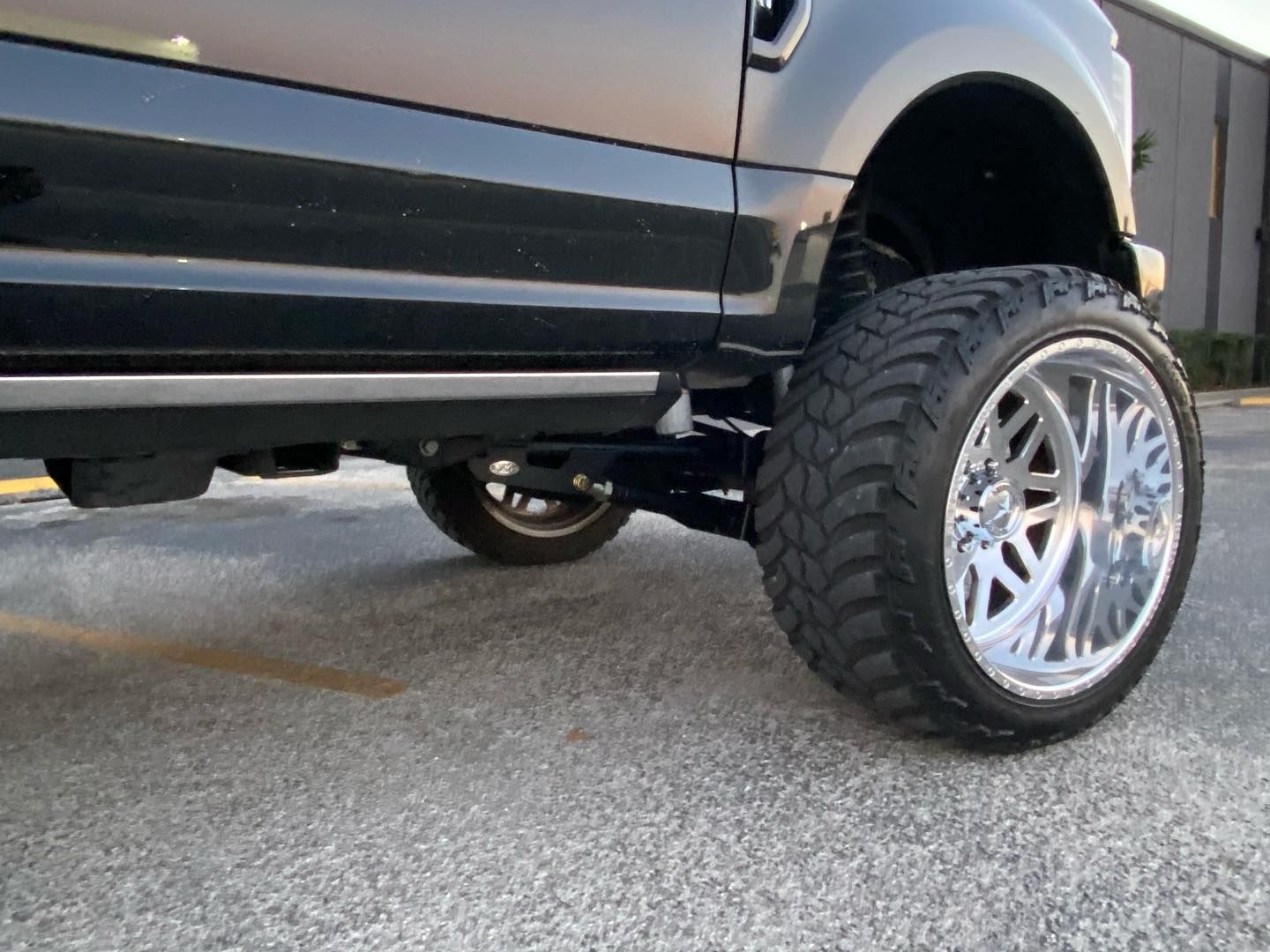 Lifted silver SUV with chrome wheel on pavement, low-angle view of the front side.