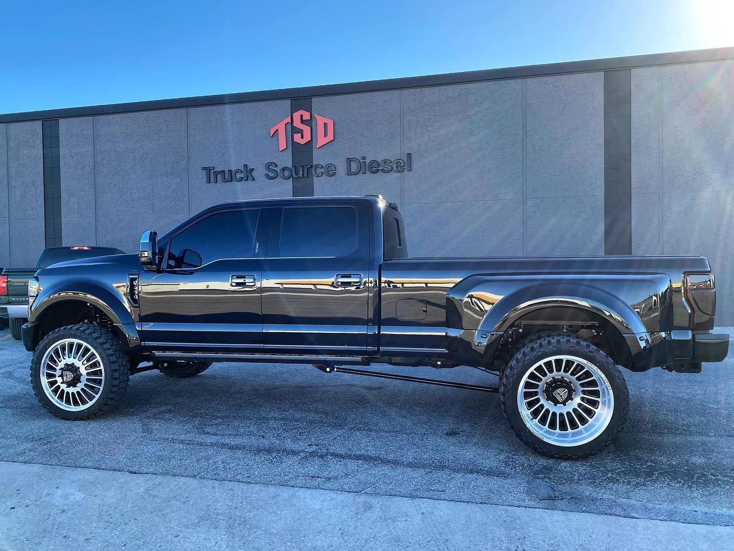 Black lifted pickup truck parked outside a diesel shop with a blue sky background
