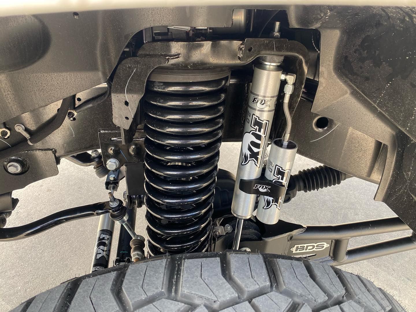 Front suspension with coil spring and shock absorber behind a tire in a vehicle wheel well