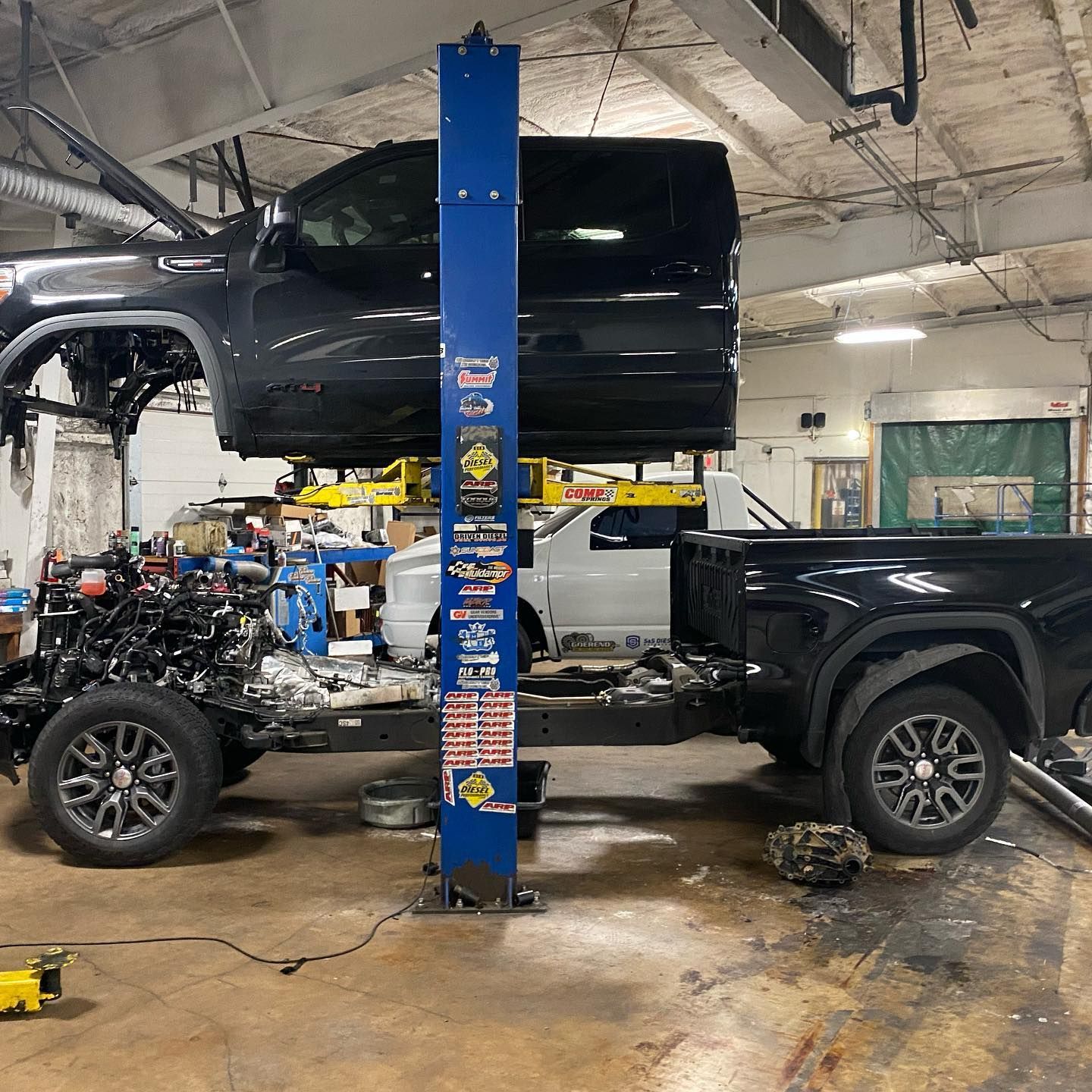Black pickup truck on a lift in an auto shop, with the engine exposed and the cab bed removed.