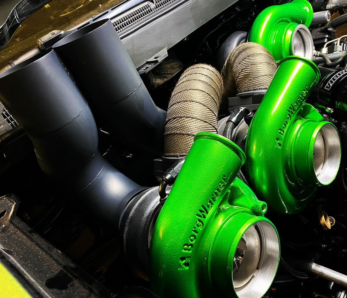 Close-up of bright green turbochargers and black piping in an engine bay