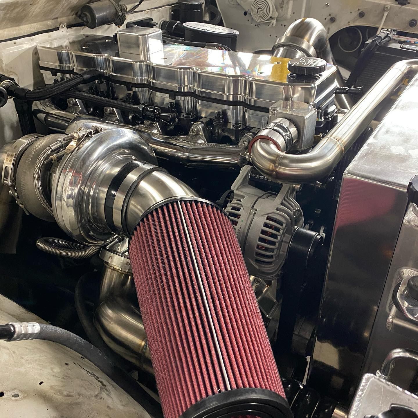 Close-up of a car engine with a red cone air filter and chrome intake pipes.