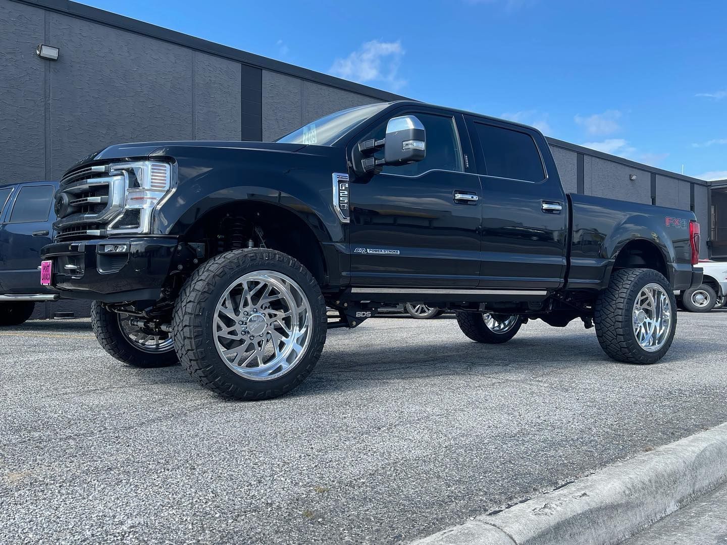 Black lifted pickup truck parked by a building on gravel, side view