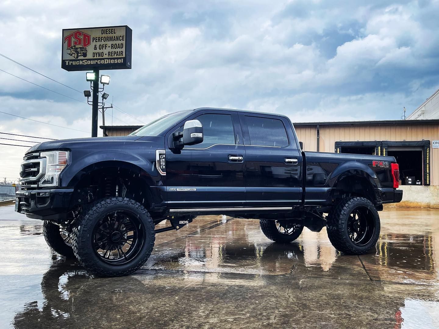 Black lifted pickup truck parked on a wet lot under a cloudy sky