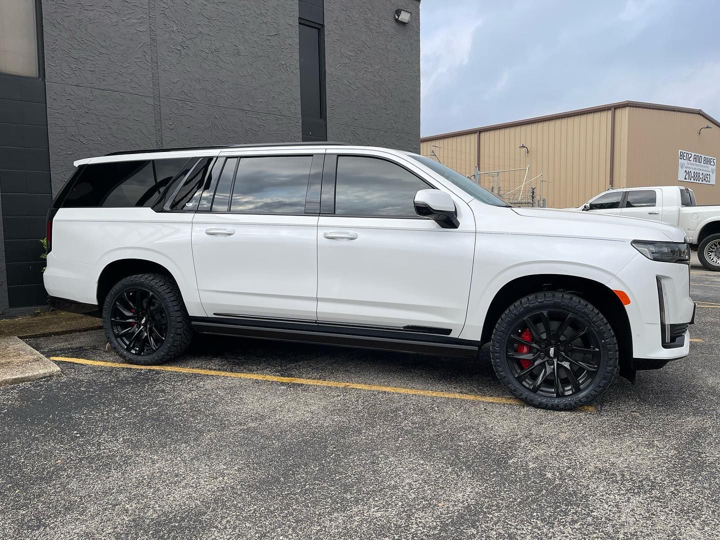 White SUV parked beside a gray building on a gravel lot, with black wheels and tinted windows