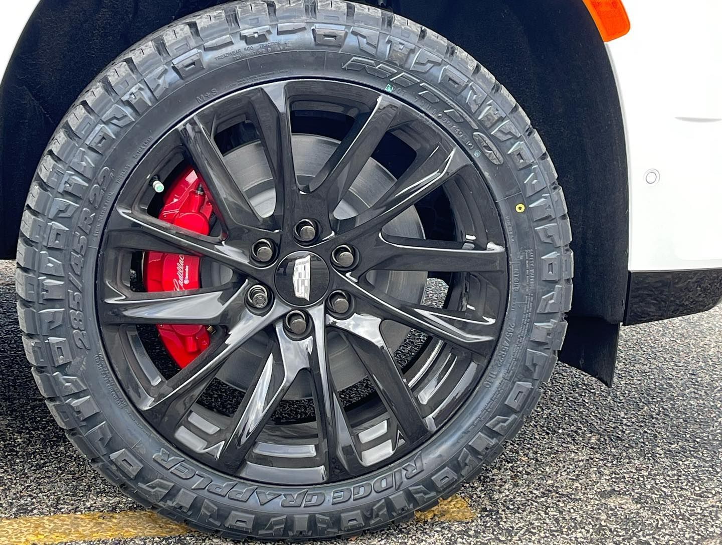Close-up of a black alloy car wheel with red brake caliper on a white vehicle.