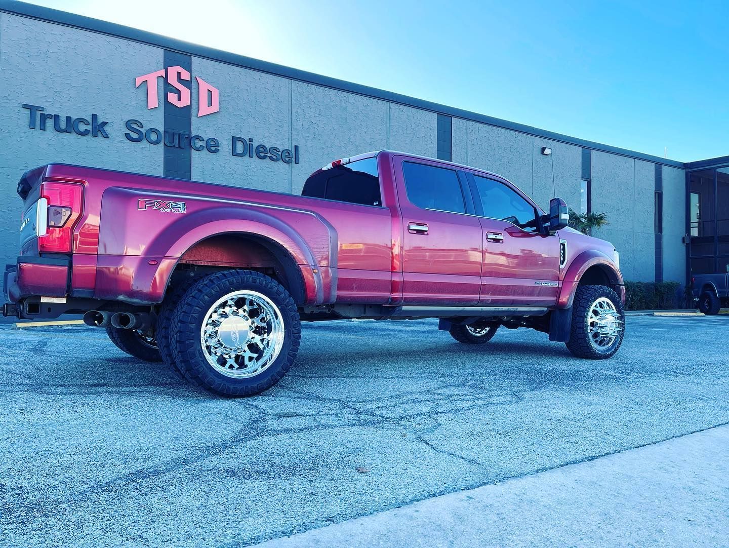 Maroon lifted pickup truck parked outside a truck service building