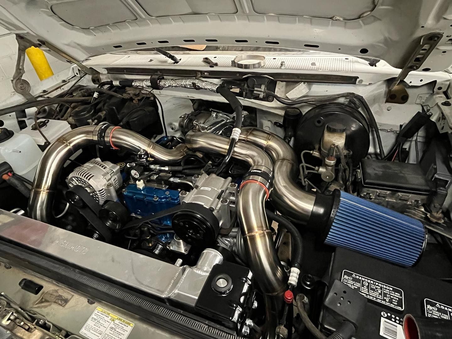 Modified car engine bay with polished turbo piping and blue air filter in a white chassis